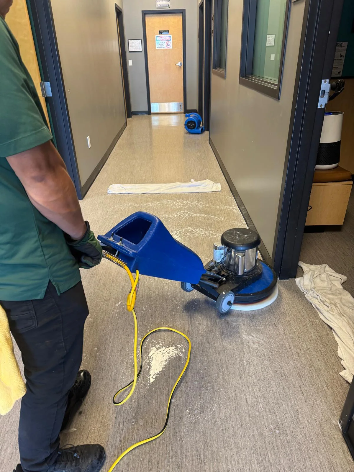 Technician operating a rotary floor cleaning machine in a commercial corridor